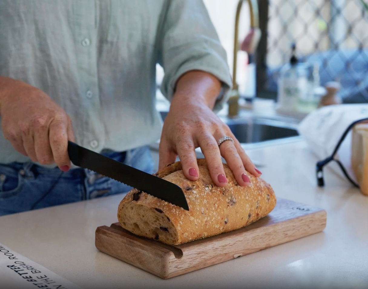 Video comparing a bread knife and a Little Bread Winner bread saw slicing a loaf — the saw cuts cleanly without squashing the bread"