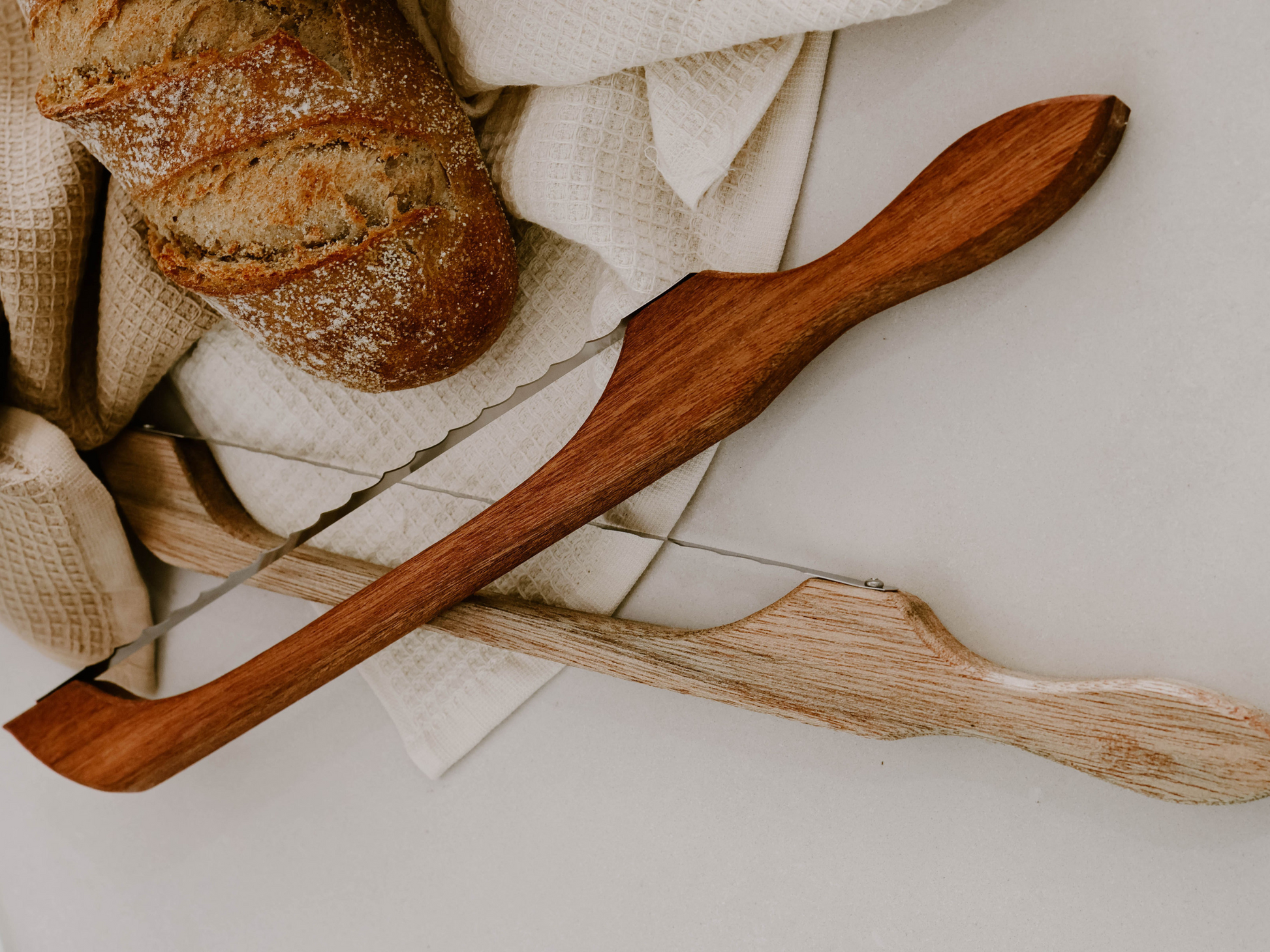 Handmade Little Bread Winner timber bread saw displayed on a wooden bench next to a fresh sourdough loaf
