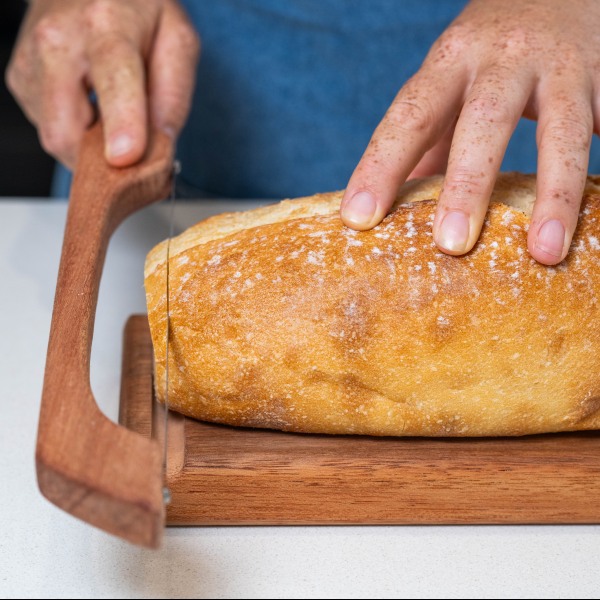 Slicing fresh crusty sourdough on a wooden bread board.