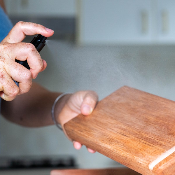 Spraying sterliser on a wooden cutting board for maintenance.