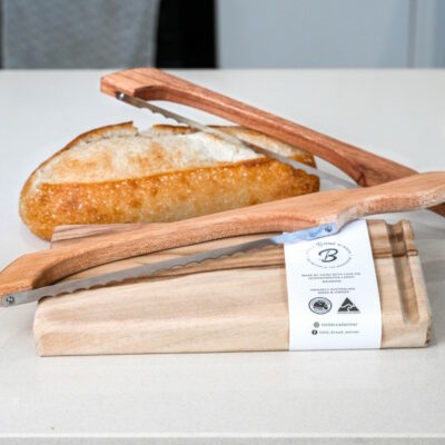 Wooden bread saw with timber cutting board and with loaf of bread on kitchen counter.