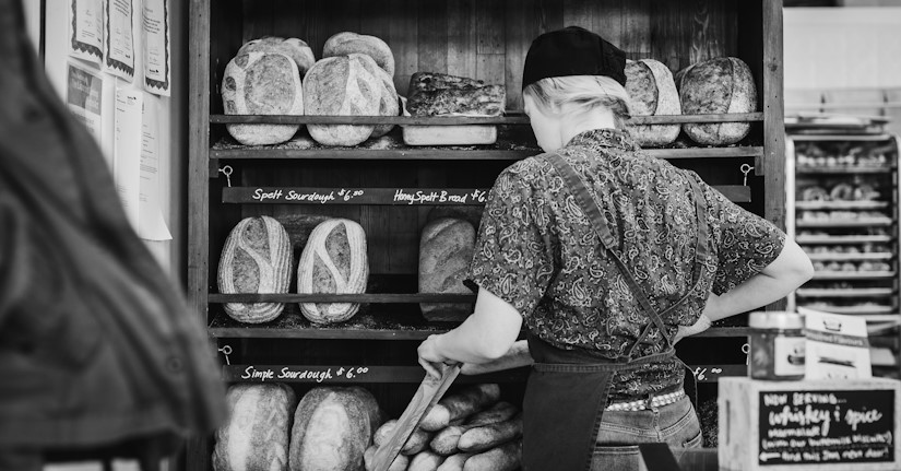 Baker stocking fresh sourdough bread on shelves.
