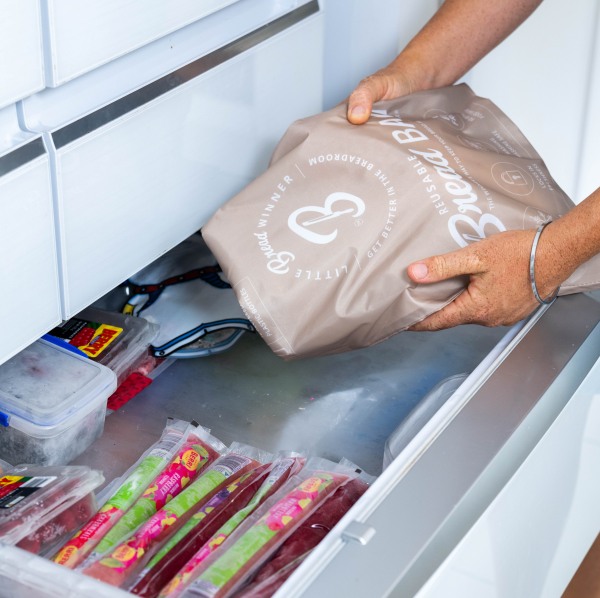 Person placing reusable bread bag in a freezer drawer with other frozen food bags and containers.